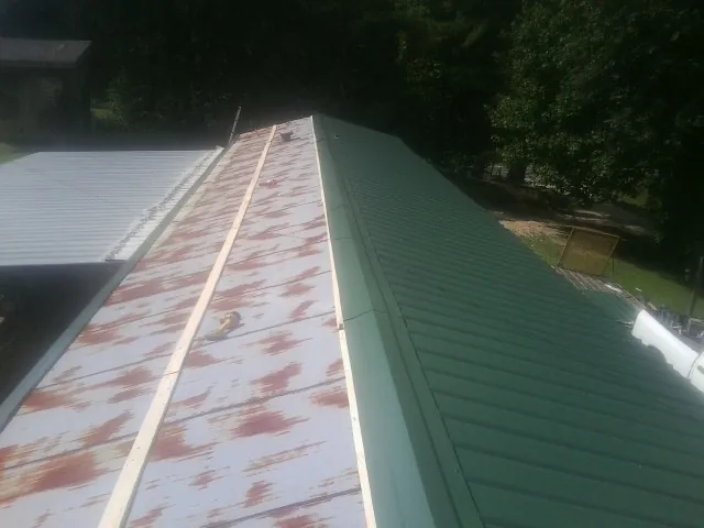 Old rusted panels beside newly installed green metal roofing — Wind Damage Roof Repair by Roofing Brothers in Decker
