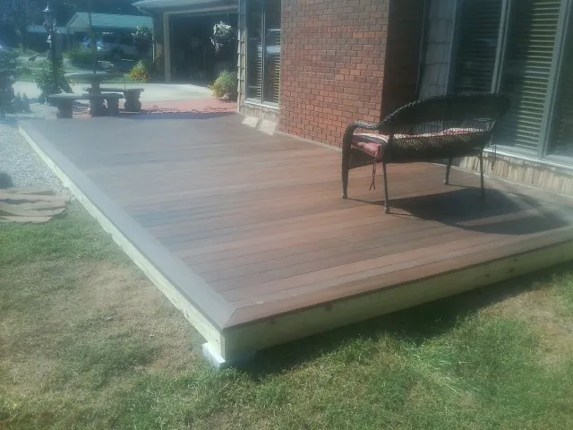 New wood deck and wicker chair beside a brick house in Decker