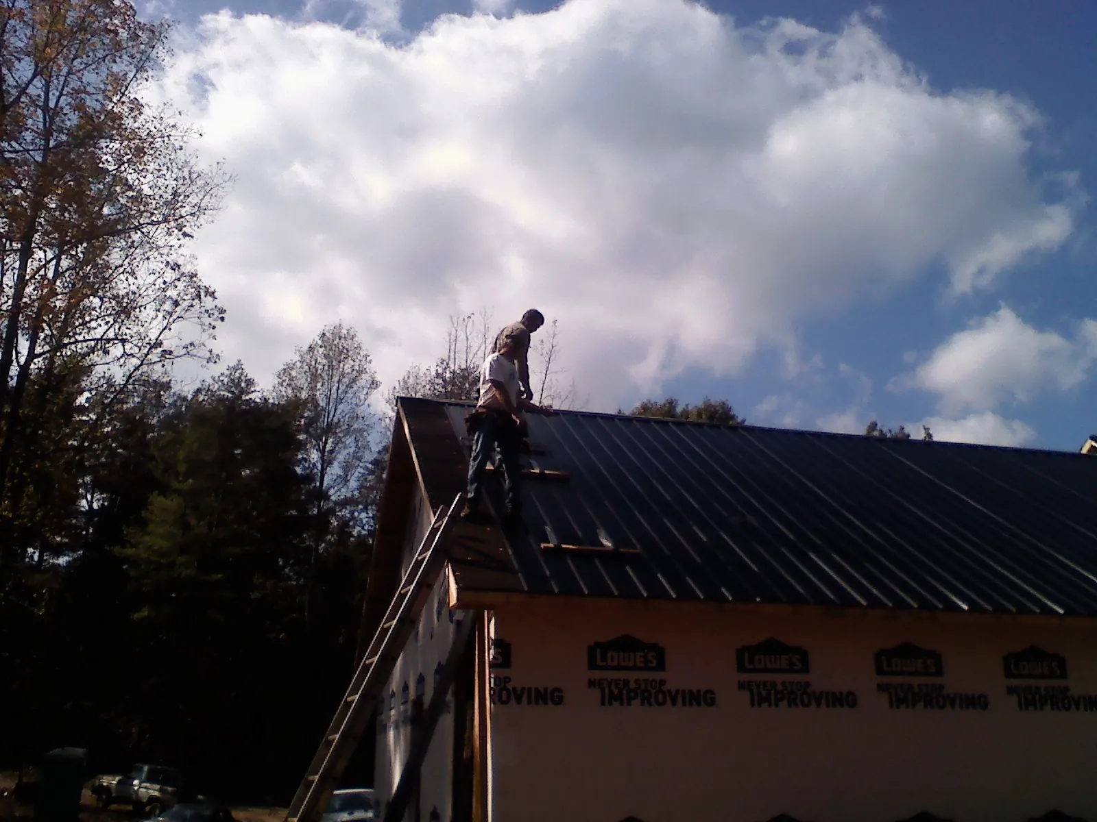 Roofer fastening dark metal panels high against a cloudy sky, from a Roof Inspection job in Decker