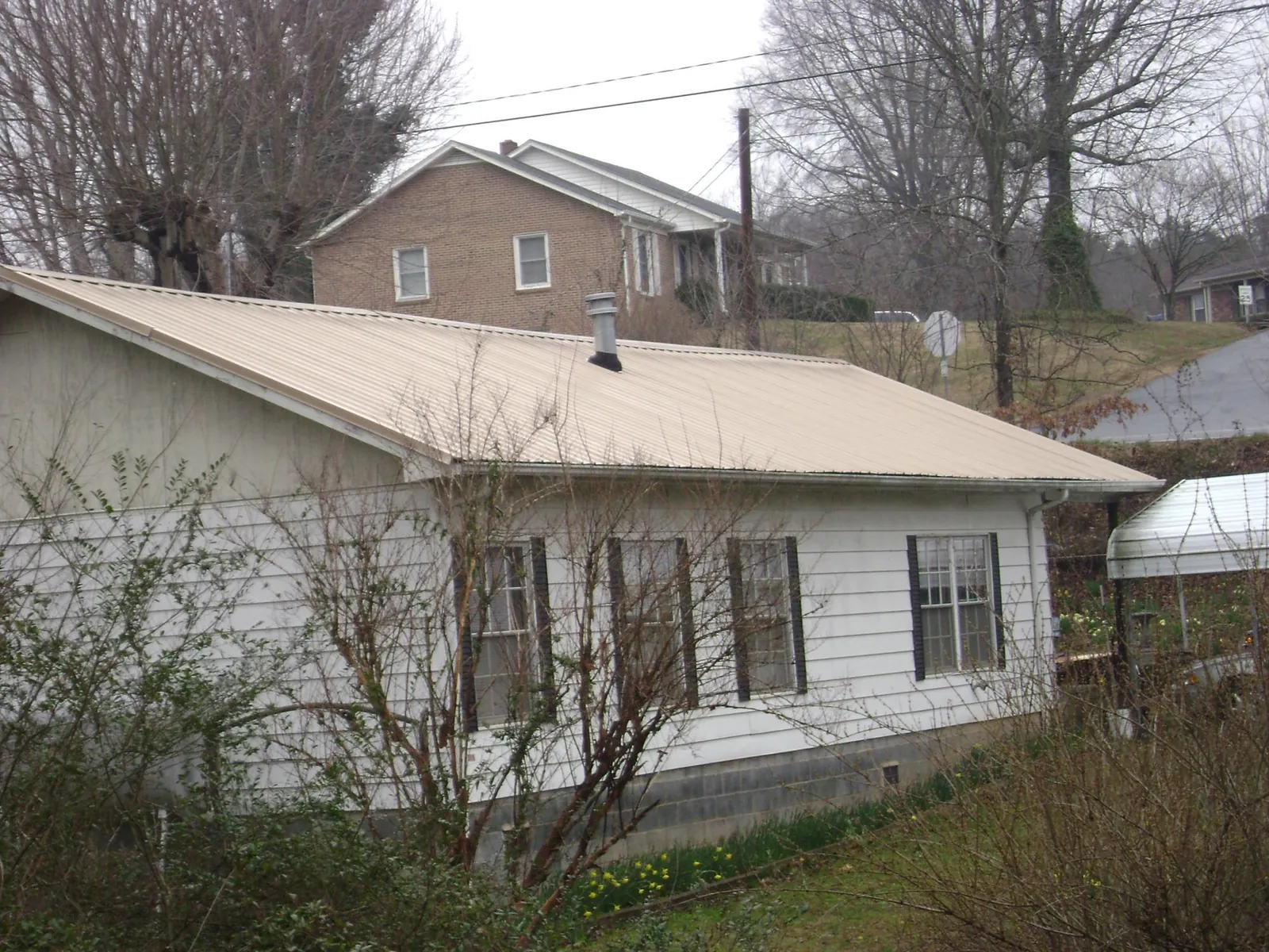 Tan metal roof on a white sided house set into a hillside — Commercial Roofing by Roofing Brothers in Decker