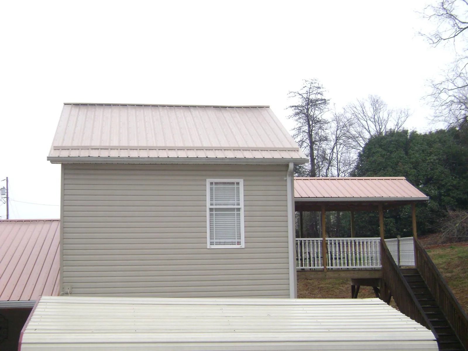 Tan metal roofs on a two story addition and attached porch, from a Roof Replacement job in Decker